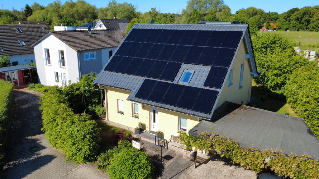 Photovoltaik Referenz – gelbes Einfamilienhaus mit Solarmodulen, Straßenansicht